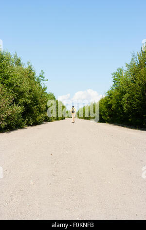 Blick von der Rückseite. Ein Mann mit einem Rucksack geht auf den Sandweg. Reisende Stockfoto
