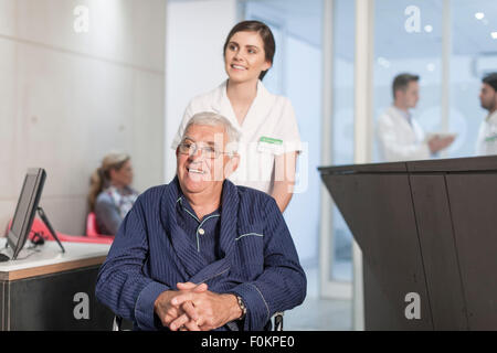 Krankenschwester mit Patienten im Rollstuhl an der Rezeption der Klinik Stockfoto