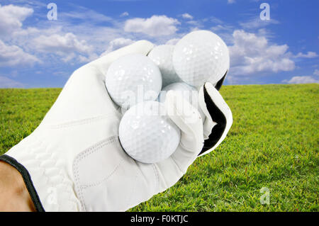 Hand hält mehrere Golfbälle mit einem schönen blauen Himmel und grünen Rasen im Hintergrund Stockfoto