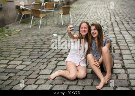 Zwei lustige Mädchen im Teenageralter machst Selfie am Telefon sitzt auf dem Bürgersteig. Stockfoto