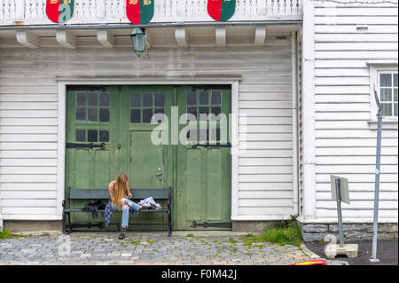 Frau mit dem Handy telefonieren, beim Sitzen auf einer Bank vor einem Holzgebäude. Stockfoto