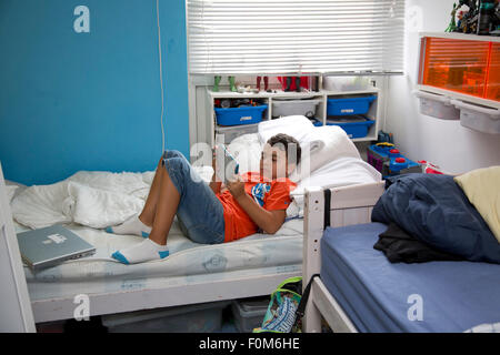 Junge auf seinem Bett, Blick auf seinen Tablet allein liegen. Stockfoto