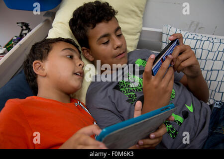 Zwei Brüder, die auf ihre Spiele-Konsolen drinnen spielen Stockfoto