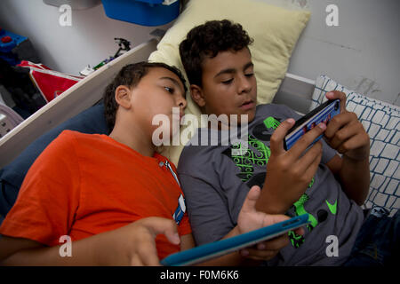 Zwei Brüder, die auf ihre Spiele-Konsolen drinnen spielen Stockfoto
