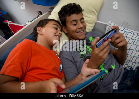 Zwei Brüder, die auf ihre Spiele-Konsolen drinnen spielen Stockfoto