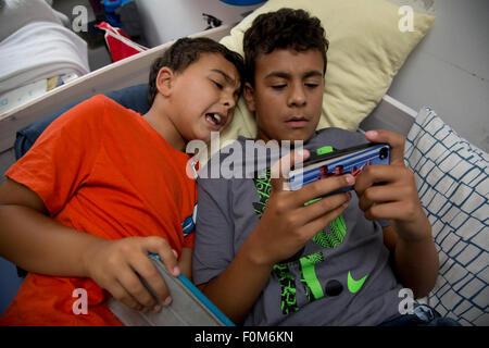 Zwei Brüder, die auf ihre Spiele-Konsolen drinnen spielen Stockfoto