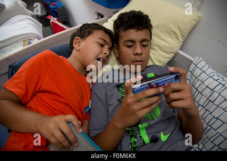 Zwei Brüder, die auf ihre Spiele-Konsolen drinnen spielen Stockfoto