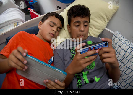 Zwei Brüder, die auf ihre Spiele-Konsolen drinnen spielen Stockfoto