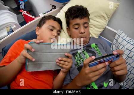 Zwei Brüder, die auf ihre Spiele-Konsolen drinnen spielen Stockfoto