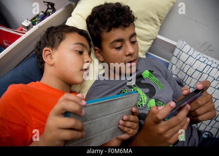 Zwei Brüder, die auf ihre Spiele-Konsolen drinnen spielen Stockfoto