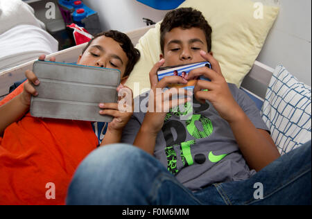Zwei Brüder, die auf ihre Spiele-Konsolen drinnen spielen Stockfoto