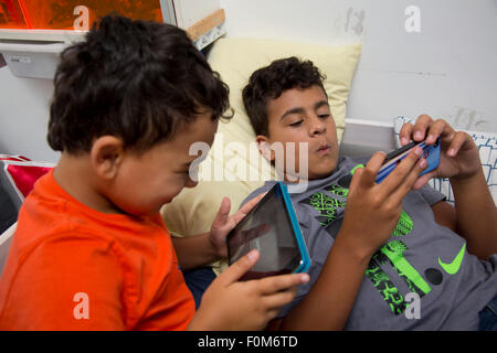 Zwei Brüder, die auf ihre Spiele-Konsolen drinnen spielen Stockfoto