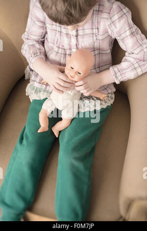 Porträt des kleinen Mädchens Plastikpuppe in ihren Händen hält. Sie sitzt in einem Sessel. Stockfoto