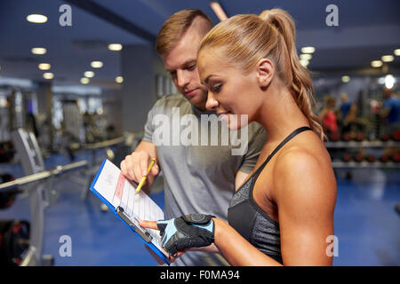 lächelnde Frau mit Trainer und Zwischenablage im Fitness-Studio Stockfoto