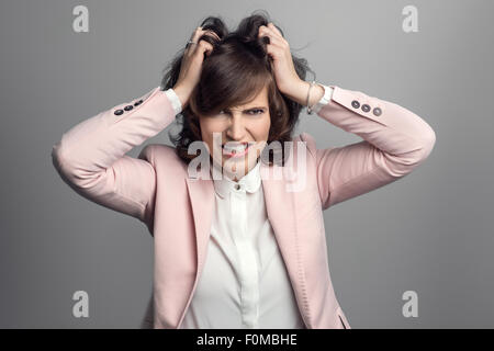 Attraktive stilvolle junge Frau in einem rosa Jacke reißen an den braunen Haaren mit ihren Händen, wie sie ihre Frustration über grau Lüftungsschlitze Stockfoto
