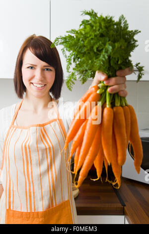 Junge Frau in ihrer Küche hält ein Bündel von Karotten Stockfoto
