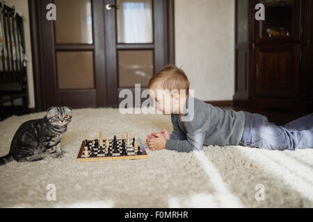 kleiner Junge spielt Schach am Boden liegend Stockfoto