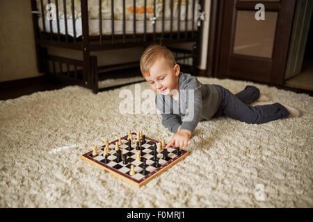 kleiner Junge spielt Schach am Boden liegend Stockfoto