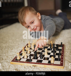 kleiner Junge spielt Schach am Boden liegend Stockfoto