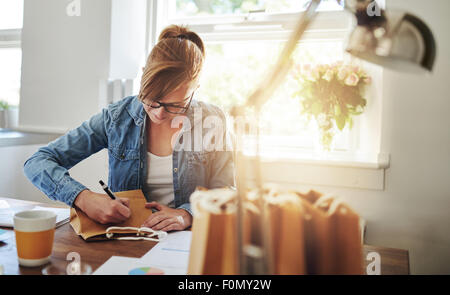 Junge Frau schreiben einige Notizen auf Papier Geschenktüte auf den Holztisch im Inneren des Hauses gegen die Glasscheibe. Stockfoto