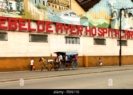 Gruppe von unbekannten Personen in einem Pferdewagen mit einer großen alten Propaganda urban Gemälde im Hintergrund. Havanna, Kuba, 2004. Stockfoto