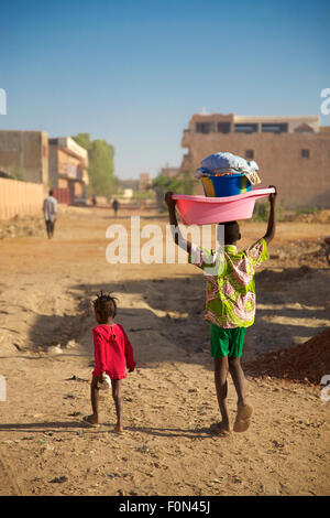 Nicht identifizierte kleines Kind zu Fuß auf der Straße mit seinem Bruder in den frühen Morgenstunden mit Wäsche auf dem Kopf in Mopti, 2010 Stockfoto