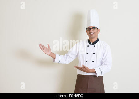 Porträt der schönen indischen männlichen Chef in Uniform Händen gestikulieren zeigt etwas und lächelnd, stehend auf einfarbigen Hintergrund Witz Stockfoto