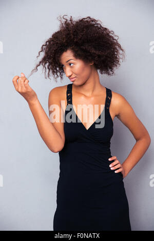 Porträt von Afro Amerikanerin im schwarzen Kleid berühren ihr Haar über grauen Hintergrund Stockfoto