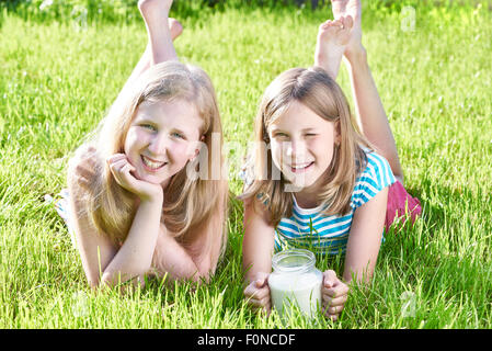 Zwei Mädchen liegen im sonnigen Wiese mit einem Krug Milch Stockfoto