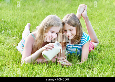 Zwei Mädchen liegen im sonnigen Wiese mit einem Krug Milch Stockfoto