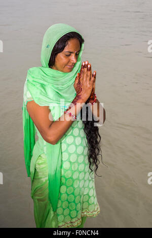 Eine junge Frau mit langen schwarzen Haaren, Henna bemalte Hände und ein grünes Kleid ist an den Ghats von dem heiligen Fluss Ganges beten. Stockfoto