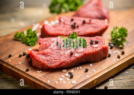 Frisches rohes Rindfleisch auf Holzbrett mit Petersilie, Pfeffer und Salz Stockfoto