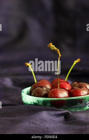 Roter Schatz Kirschen in einer rustikalen Glasschüssel auf blauem Hintergrund mit textfreiraum Seide. Selektiven Fokus. Vertikale. Stockfoto