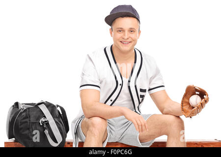 Junge Sportler mit einem Baseballhandschuh, sitzen auf einer Bank mit einer Sporttasche neben ihm und hält einen baseball Stockfoto