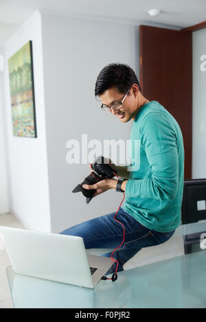 Chinesischer Mann verbindet digitale Dslr-Kamera, Laptop-Computer über USB-Kabel, Fotos und Videos auf dem PC und lächelnd. Die g Stockfoto