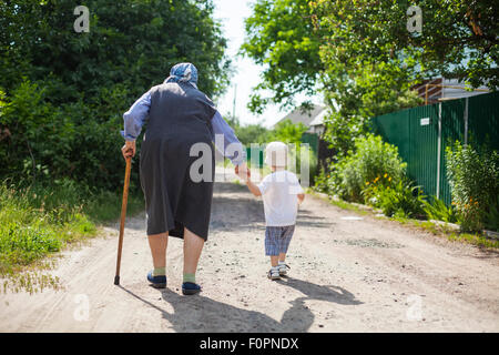 Große Großmutter und Kleinkind Jungen Hand in Hand beim gehen auf der Straße in Landschaft Stockfoto