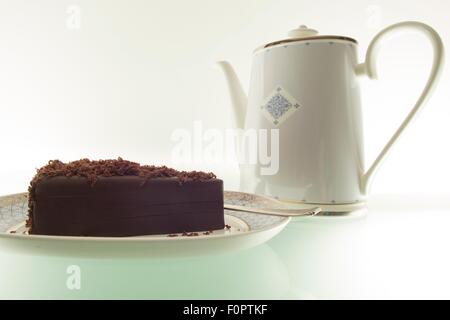 Ein Kuchen, Schokolade und einer Teekanne auf einem Tisch grünes Licht aus. Stockfoto