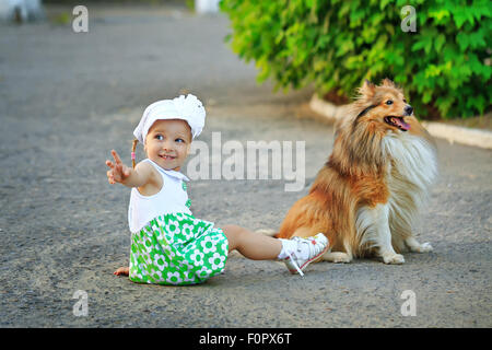 Kleines Mädchen und ein Hund auf dem Boden saßen. Girl zeigt irgendwo Zeigefinger. Stockfoto