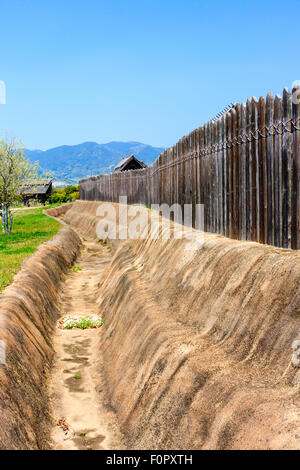 Japan, Yoshinogari Eisenzeit Historical Park. Rekonstruierte Yayoi Gehäuse. Äußere Holz- beteiligung Verteidigungsmauer mit dugout Graben. Stockfoto