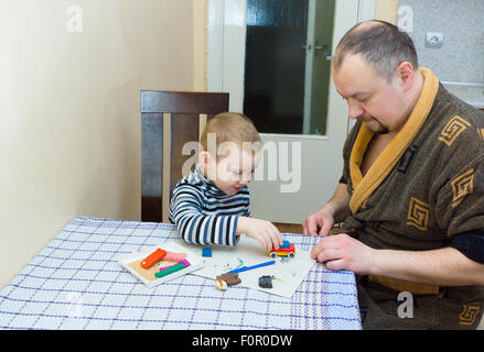der Vater und der Sohn sitzen an einem Tisch und sind dabei, ein Formteil aus Farbe Plastilin Stockfoto
