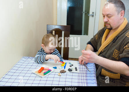 der Vater und der Sohn sitzen an einem Tisch und sind dabei, ein Formteil aus Farbe Plastilin Stockfoto