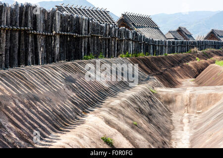 Japan, Yoshinogari Eisenzeit Historical Park. Rekonstruierte Yayoi Gehäuse. Äußere Holz- beteiligung Verteidigungsmauer mit dugout Graben. Stockfoto