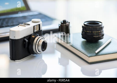 35mm Vintage Fotokamera auf Tisch in der Nähe von Objektiv, Film und notebook Stockfoto