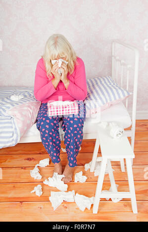 Kranke Dame mit rosa Pyjama und Gewebe sitzt auf ihrer Nase zu Bett Stockfoto