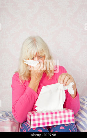 Traurige Frau mit rosa Pyjama und Gewebe sitzt auf ihrer Nase zu Bett Stockfoto