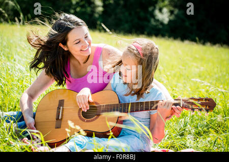 Mutter lehrt Plaing Gitarre ihr Kind - in der Natur an sonnigen Tag im freien Stockfoto