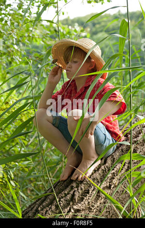 kleiner Junge verkleidet als Huckleberry Finn sitzt in einem Baum seine Pfeife rauchen Stockfoto