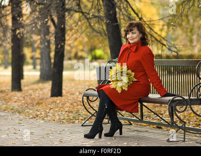 Die Reife schöne Frau im roten Mantel, outdoor im Park, Herbsttag Stockfoto