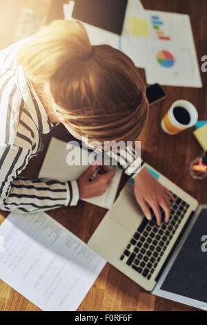 Fleißige erfolgreiche weibliche Unternehmer arbeiten an ihrem Schreibtisch in Ihrem Büro zu Hause schreiben, da sie neue Märkte auf Forschungen Stockfoto