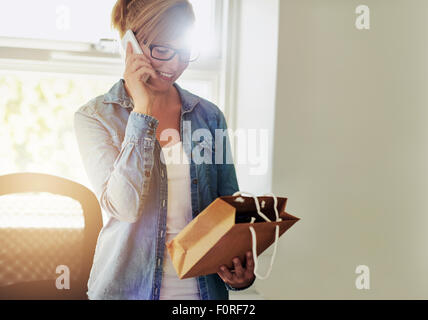 Junge Geschäftsfrau im Chat am Telefon, wie sie in ihre neue e-Business als sie Verpackungen für Produkte zum Verkauf diskutiert Stockfoto